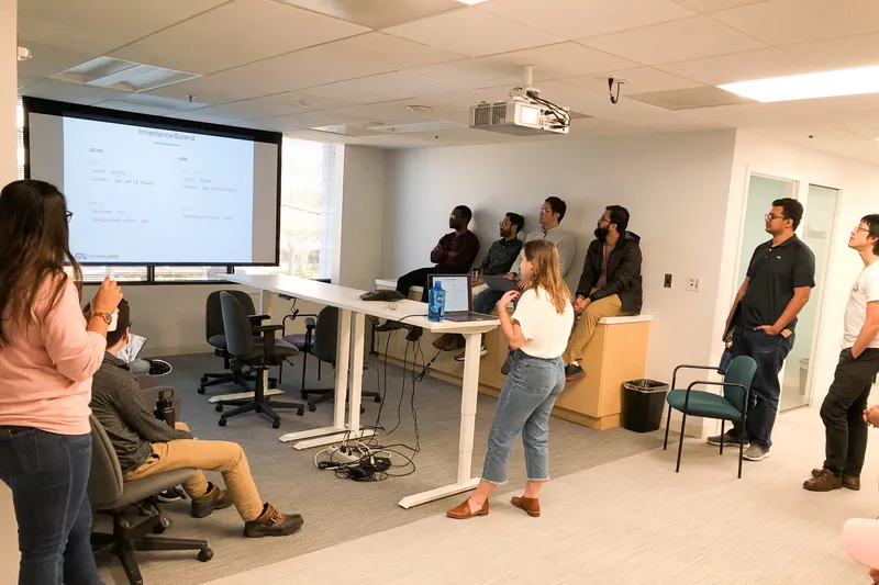 EAi teammates gathered in a conference room, watching a presentation on a projector screen.